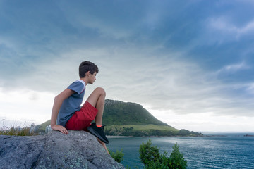 Fototapeta na wymiar Boy sits on rock looking out to sea