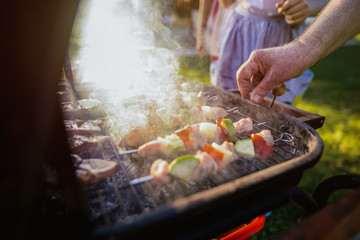 Close up of males hand turning meat and vegetable on barbeque grill.