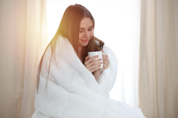 Woman wrapped in a blanket and holds a mug after wake up, entering a day happy and relaxed after good night sleep. Sweet dreams, good morning, new day, weekend, holidays concept