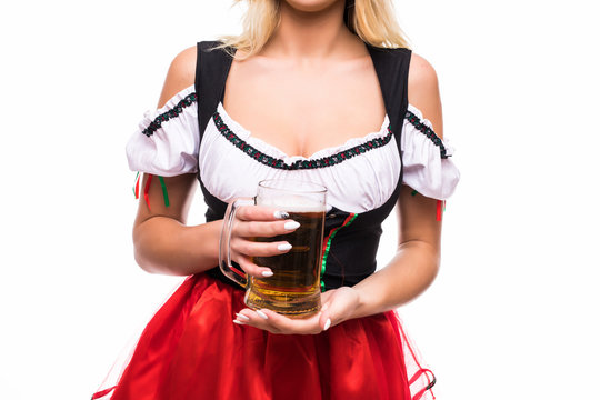 Cropped studio close up of a sexy big breasted bavarian girl in dirndl dress holding mug of beer and pretzel isolated on white. Oktoberfest waitress serving drinks.