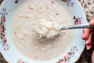 Oatmeal with fruit in a plate and a hand takes a spoonful of porridge.