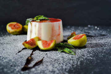Panna cotta dessert with fresh fig fruits, jam and mint leaves on dark background. Copy space