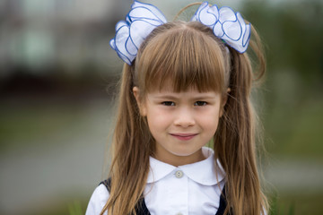 Close-up portrait of cute adorable smiling little first grader girl in school uniform and white...