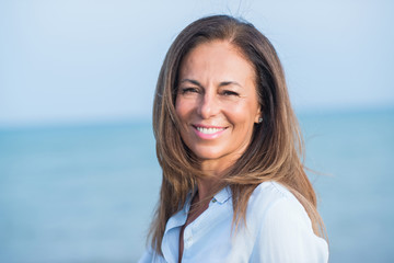 Beautiful middle age hispanic woman standing with smile on face at the ocean. Smiling confident and...