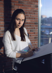 girl designer sitting on a chair by the window and draws a sketch works as an artist