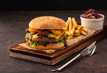 Juicy homemade cheeseburger in a black bun with onion rings and dried tomatoes. Beef Burger with...