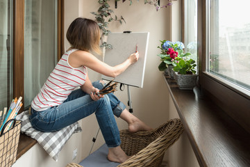 A female artist painting on canvas on her studio balcony.
