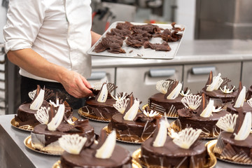 Pastry Chef decorating chocolate cakes in the kitchen of pastry shop .