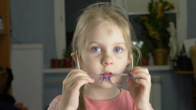 Little blue-eyed kid with blond hair with eyeglasses has eyesight problems. She is rubbing his nose and eyes because of weariness