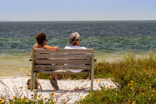 Two women sit on bench and talk at shoreline