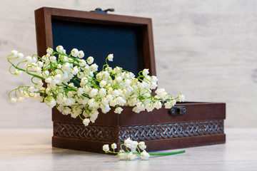 Bouquet of fresh lily of the valley flowers in small casket on light wooden background. Beautiful spring still life, copy space