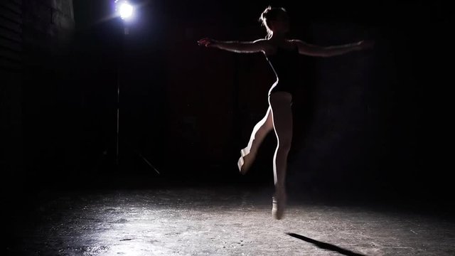 Professional graceful flexible ballerina dancing on her pointe ballet shoes in spotlight on black background in studio. Ballet dancer shows classic ballet pas wearing tutu and pointe shoes. Slow