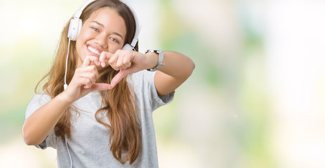 Young beautiful woman wearing headphones listening to music over isolated background smiling in love showing heart symbol and shape with hands. Romantic concept.