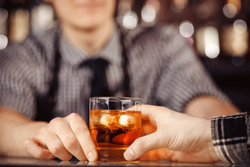 Barman holds out glass of whiskey with ice to male visitor. Concept rest in bar