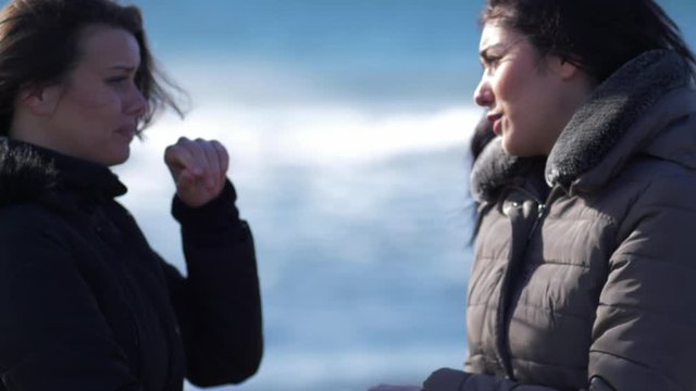 Two women crying hugging each other in winter in front of the ocean super slow motion closeup