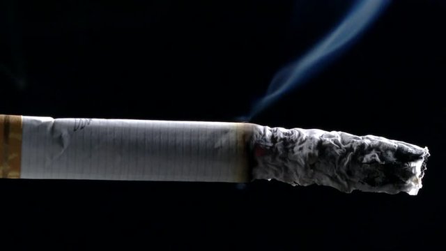 Cigarette burning in front of a black background. Extreme macro close up in Slow-motion.