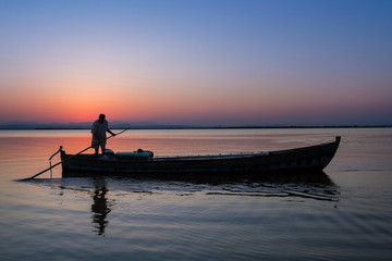 Naklejka na ściany i meble Silhouette of fisherman on a boat at dusk