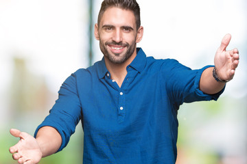 Young handsome man over isolated background looking at the camera smiling with open arms for hug. Cheerful expression embracing happiness.