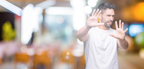 Young man wearing casual white t-shirt over isolated background afraid and terrified with fear expression stop gesture with hands, shouting in shock. Panic concept.