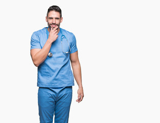 Handsome young doctor surgeon man over isolated background looking confident at the camera with smile with crossed arms and hand raised on chin. Thinking positive.