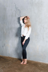 Model blonde blue jeans white shirt standing gray wall by window  copy space.