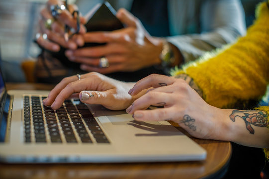 Tattooed woman hands writing and using laptop, man in background.Group of multiethnic people having business team meeting in restaurant lounge.Teamwork,corporate,diversity and social concepts.