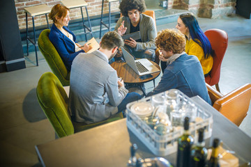 High view of colleagues working and talking at shop table.Group of multiethnic people having business team meeting in restaurant lounge.Teamwork,corporate,diversity and social concepts.