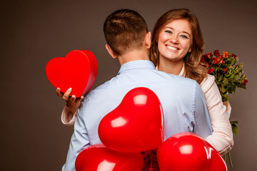 Young couple with heart shaped red balloons near grey wall