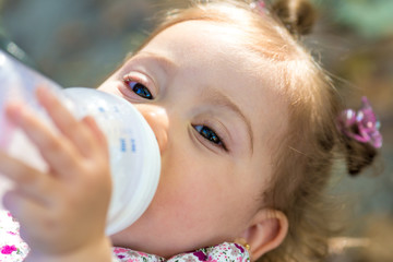 Little child drinking milk from baby bottle outdoors.