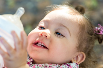 Little child drinking milk from baby bottle outdoors.