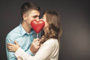 Young couple with heart shaped red balloons near grey wall
