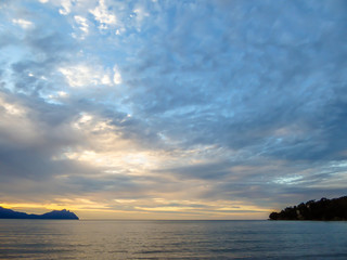 Naklejka na ściany i meble Beautiful formation of clouds over the sea in Bako National Park, Borneo, Malaysia during the sunset. Blue and yellow sky. Two islands visible on both sides of the picture. Overcast. 