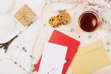 Mockup with a cup of tea, cookies with chipped chocolade, present box, little eiffel tower, blank page for writing a letter, envelope, red diary, white pen and little eiffel tower on fabric background