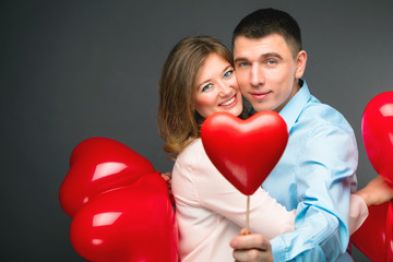 Fototapeta na wymiar Young couple with heart shaped red balloons near grey wall