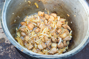 Meat and onions are roasted in a cauldron for a pilaf