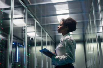 Medium shot of female technician working on a tablet in a data center full of rack servers running diagnostics and maintenance on the system