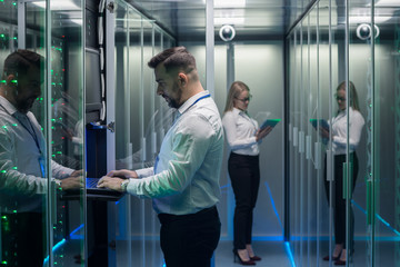 Side view of man and woman with tablet diagnosing server hardware opening glass door of rack in data center corridor