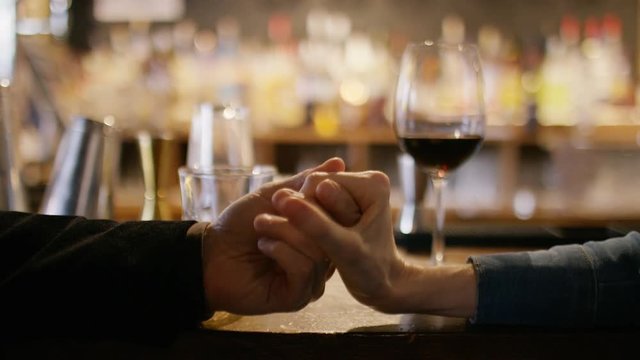 Hands of a couple holding each other in a wine bar next to their drinks
