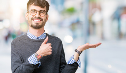 Young handsome smart man wearing glasses over isolated background Showing palm hand and doing ok gesture with thumbs up, smiling happy and cheerful