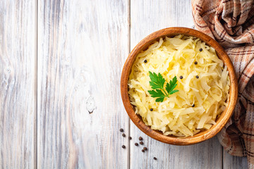 Homemade sauerkraut with black pepper and parsley in wooden bowl on rustic background. Top view....