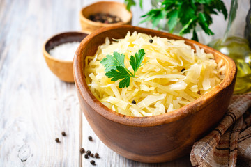 Homemade sauerkraut with black pepper and parsley in wooden bowl on rustic background. Selective focus.