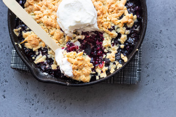 Black currant crumble with vanilla ice cream in cast iron pan. Healthy food concept. Grey stone background. Top view. Copy space.