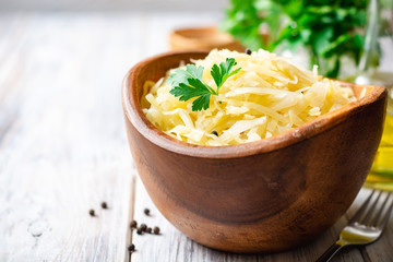 Homemade sauerkraut with black pepper and parsley in wooden bowl on rustic background. Selective focus.