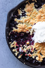 Black currant crumble with vanilla ice cream in cast iron pan. Healthy food concept. Grey stone...