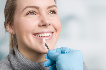 Bei einer jungen Frau wird die Zahnfarbe mit einer Zanfarbprobe ermittelt