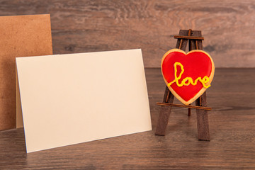 Heart with icing on the easel, with a postcard and an envelope on a wooden background