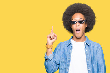 Young african american man with afro hair wearing thug life glasses pointing finger up with...