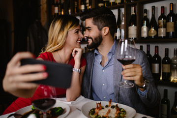 Beautiful young romantic couple taking selfie photo in restaurant during date.