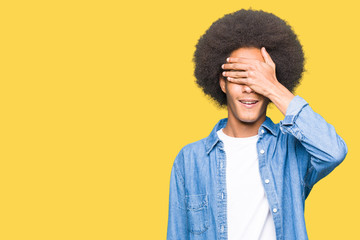 Fototapeta na wymiar Young african american man with afro hair smiling and laughing with hand on face covering eyes for surprise. Blind concept.
