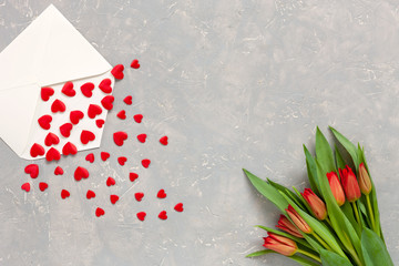 Red hearts figurines in the paper envelope and red tulips bouquet on light background. Concept for Women's Day March 8, Valentine day
